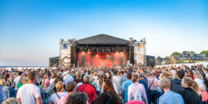 Viele Menschen vor einer Bühne bei blauem Himmel direkt am Strand